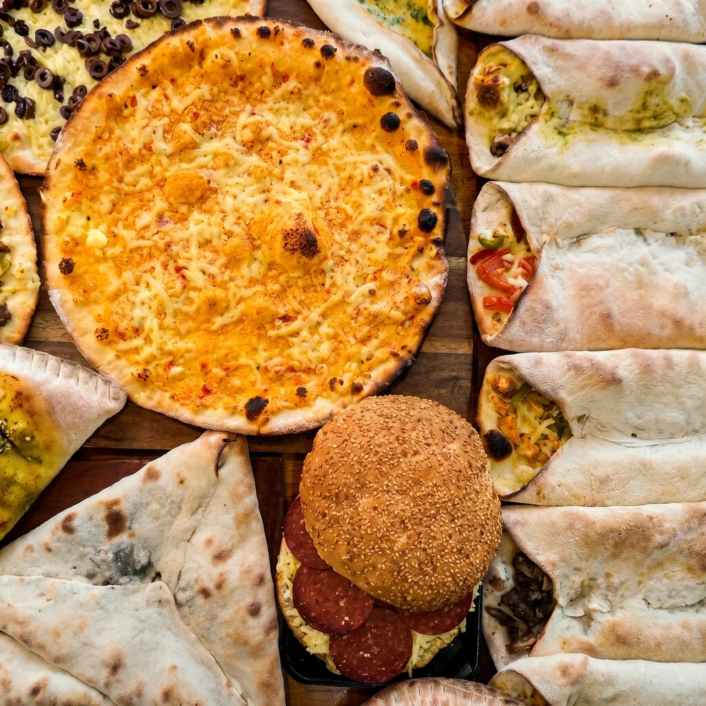 A table of pizzas, manoushe, pies, wraps and a kaak